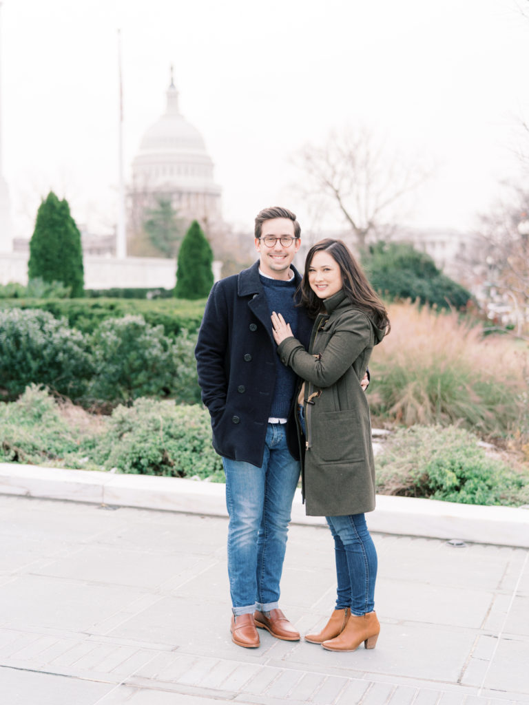 Couple smiles at the camera in the Supreme Court Gardens with the Washington DC Capitol building in the background