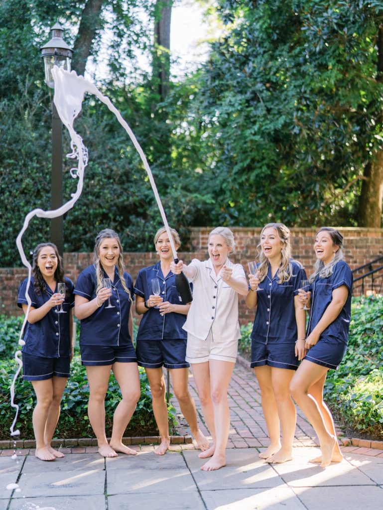 Bride and bridesmaids in dark blue robes popping champagne while they get ready for Meredith's wedding day at the Williamsburg Inn in Williamsburg Virginia