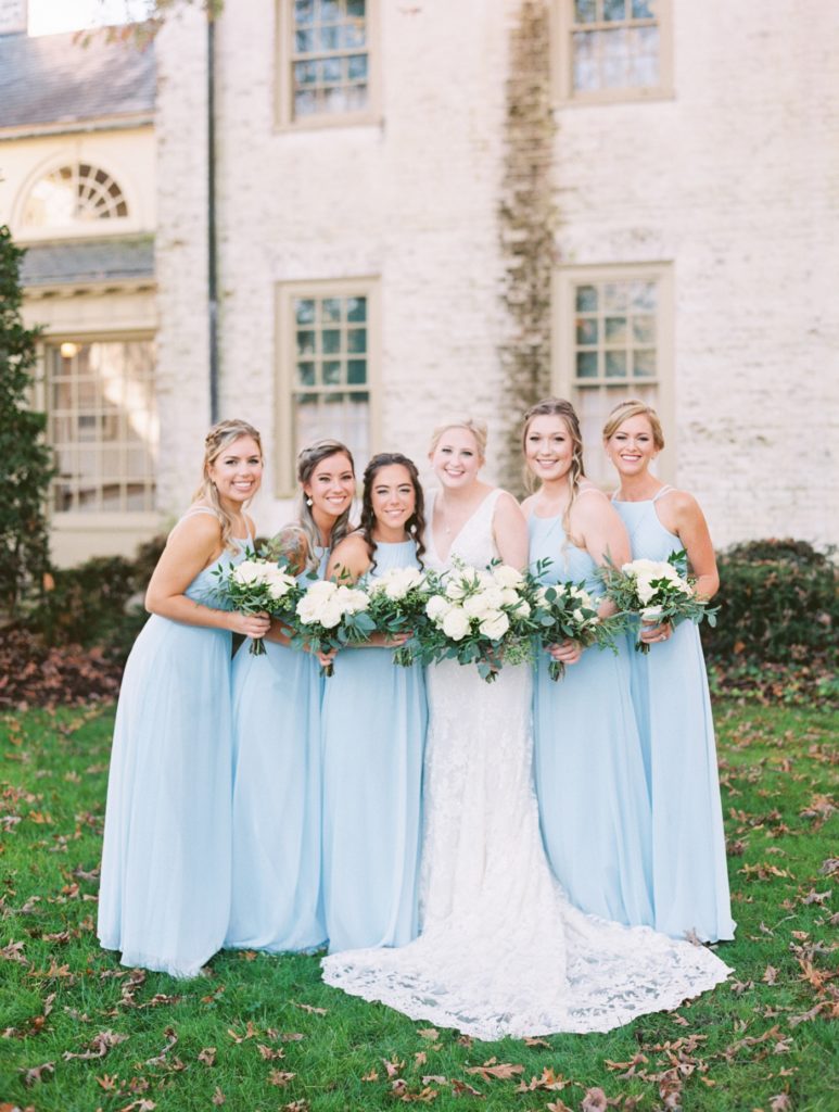 Bride and bridesmaids in light blue gowns from Azazie smiling at the camera at the Williamsburg Inn in Williamsburg Virginia