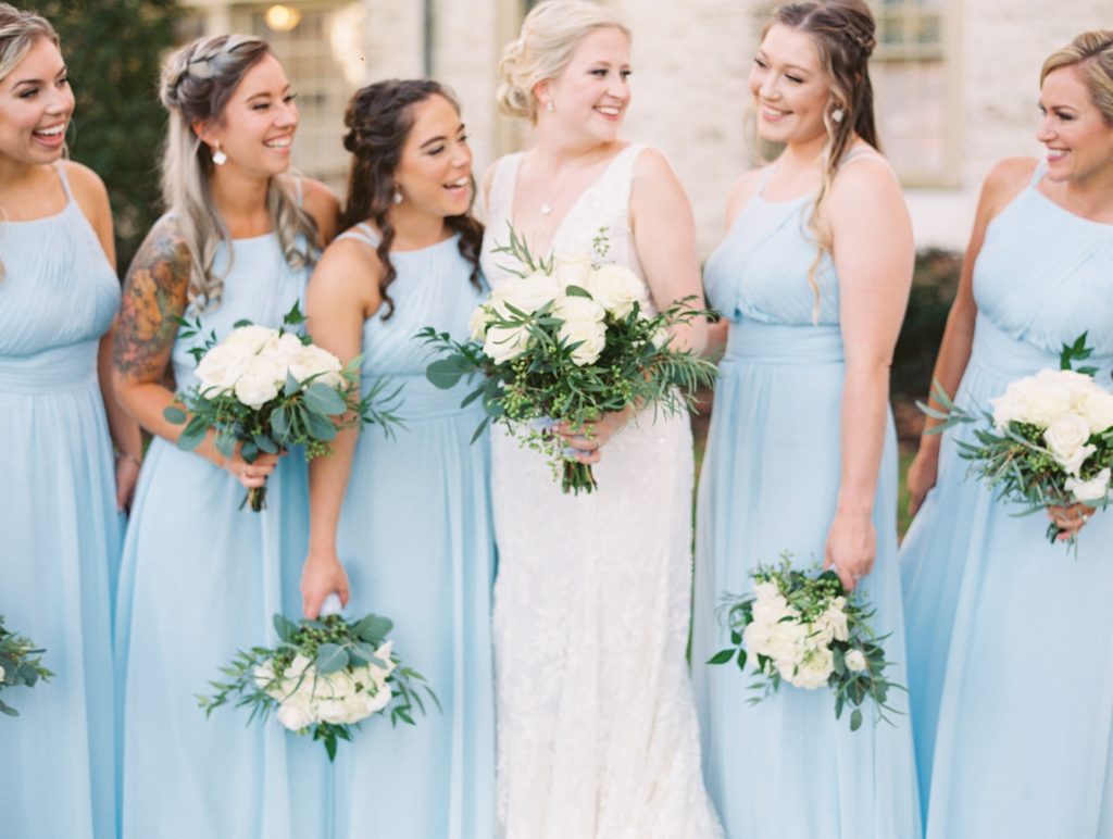 Bride and bridesmaids in light blue gowns from Azazie smiling at the camera at the Williamsburg Inn in Williamsburg Virginia