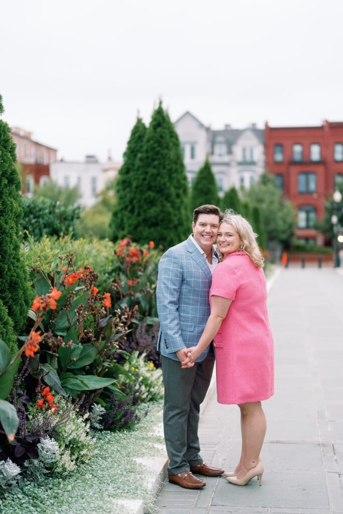 engaged Couple smiling at the camera with the capitol hill neighborhood behind them in washington dc