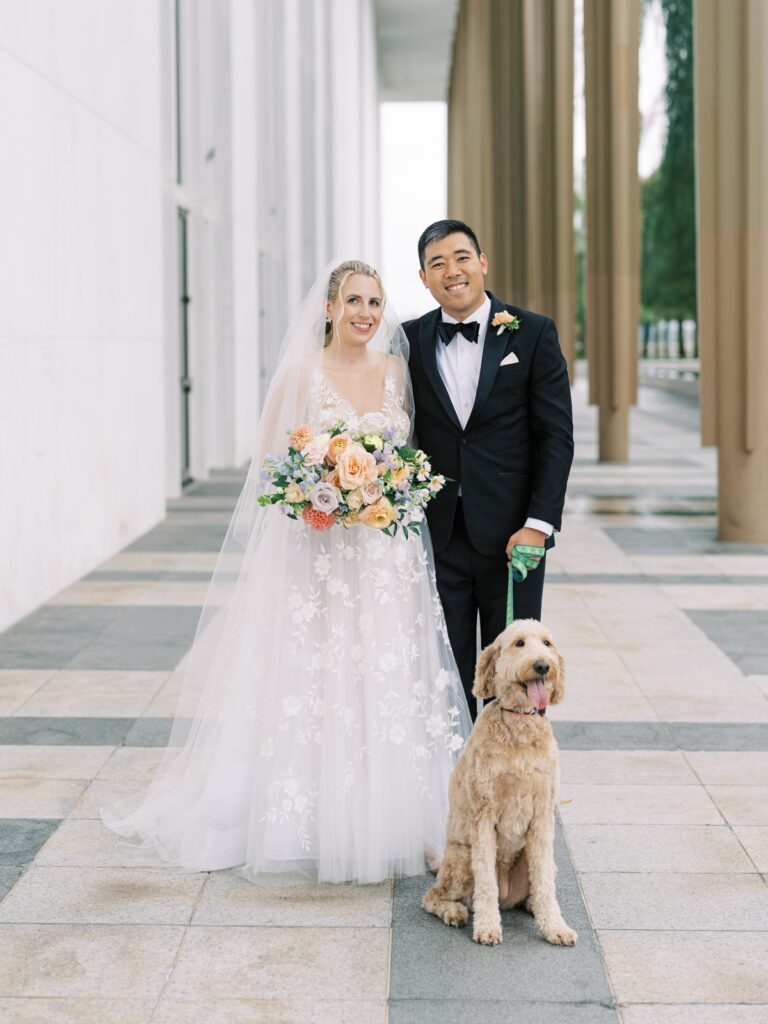 bride and groom smile at the camera with their dog at the kennedy center in washington dc
