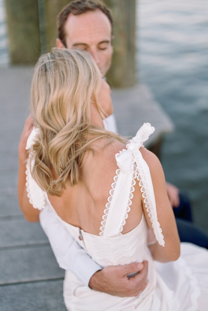 bride resting her head on groom along the waterfront